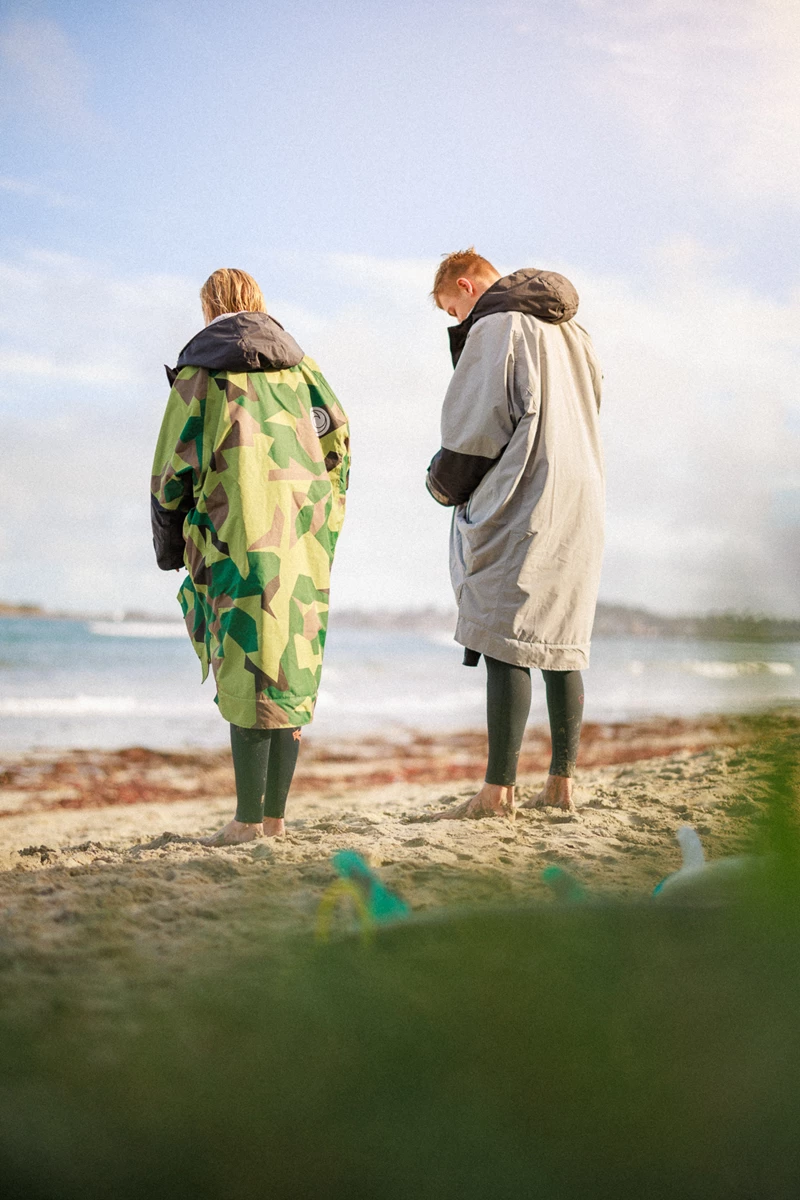 Colour photo of a man and woman standing on a beach looking at the ocean