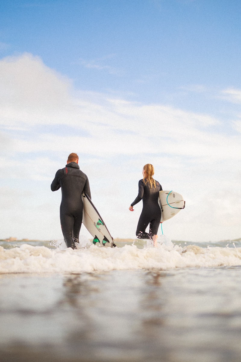 Colour photo of a couple of people walk across the water with surfboards