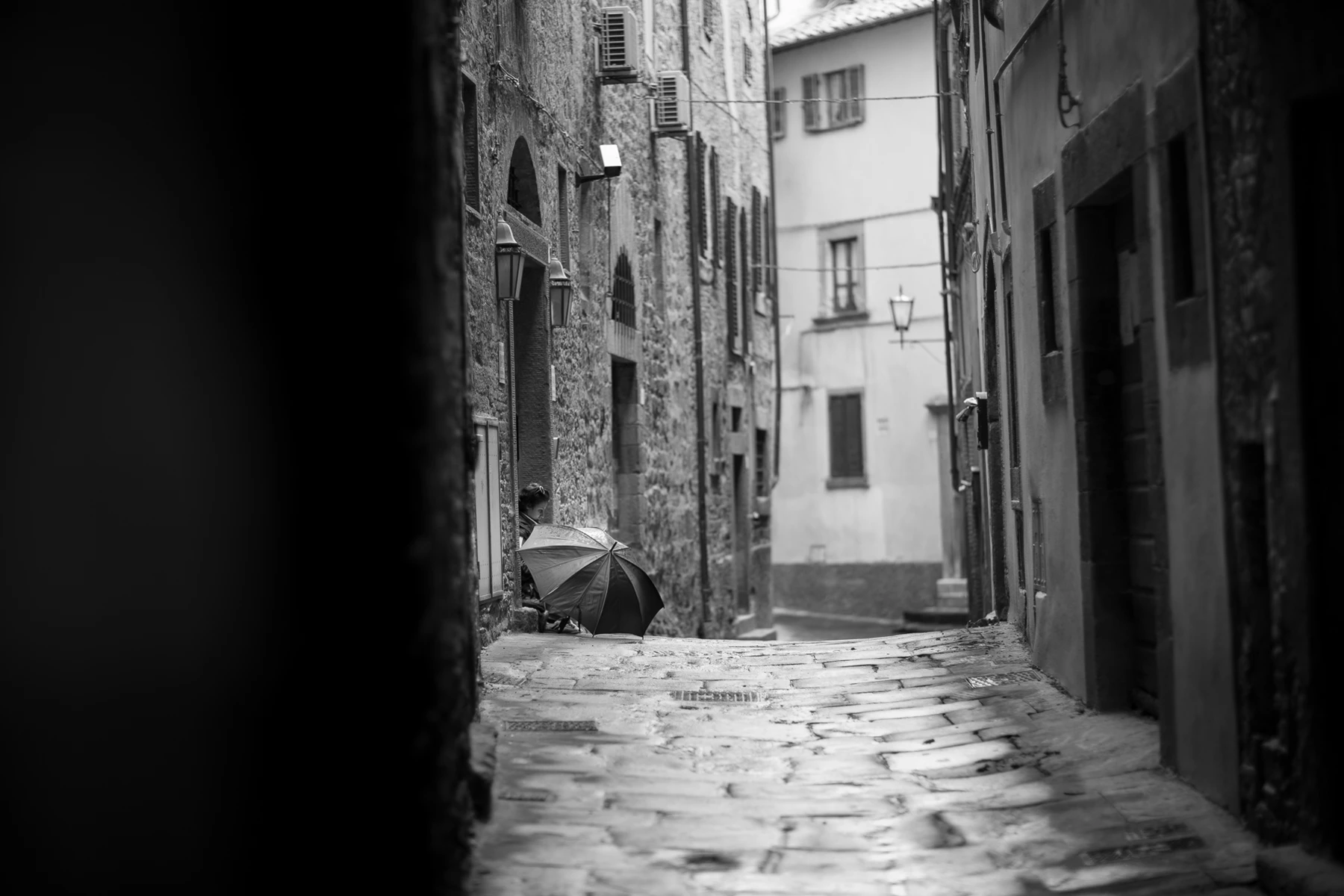 Black & white photo of a person walking down a street with an umbrella