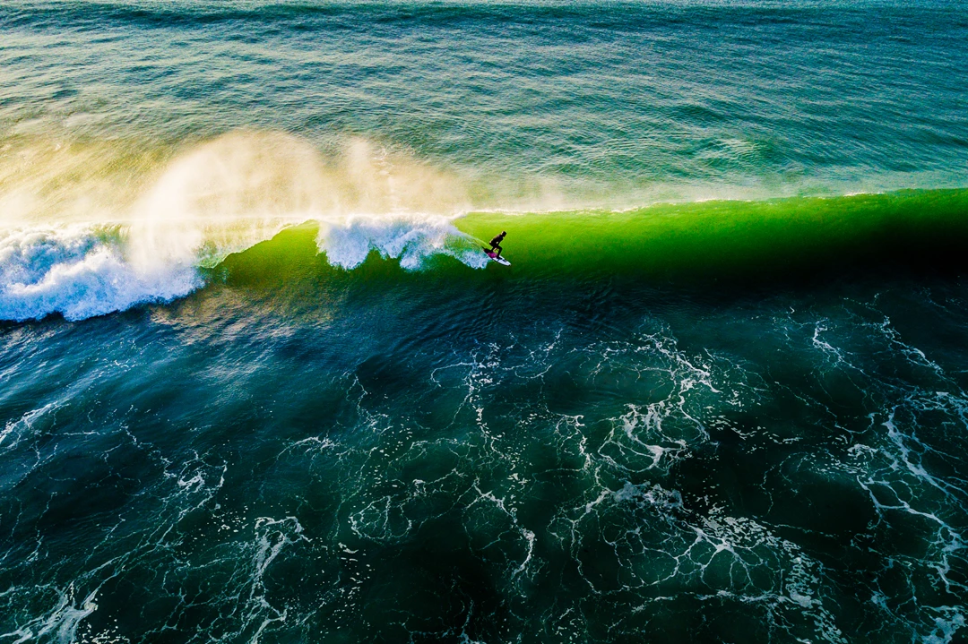 Aerial drone photo of surfer riding wave with sunlight shining through