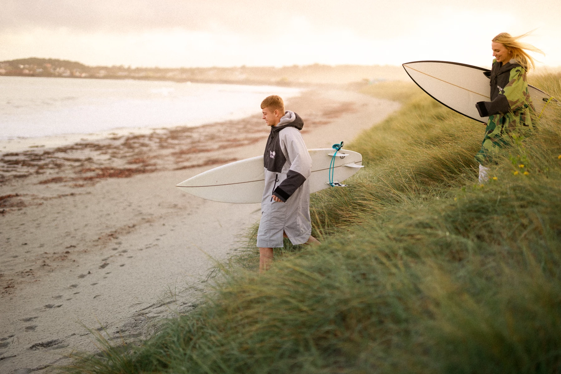 Colour photo of a couple of people walk down a beach with surfboards