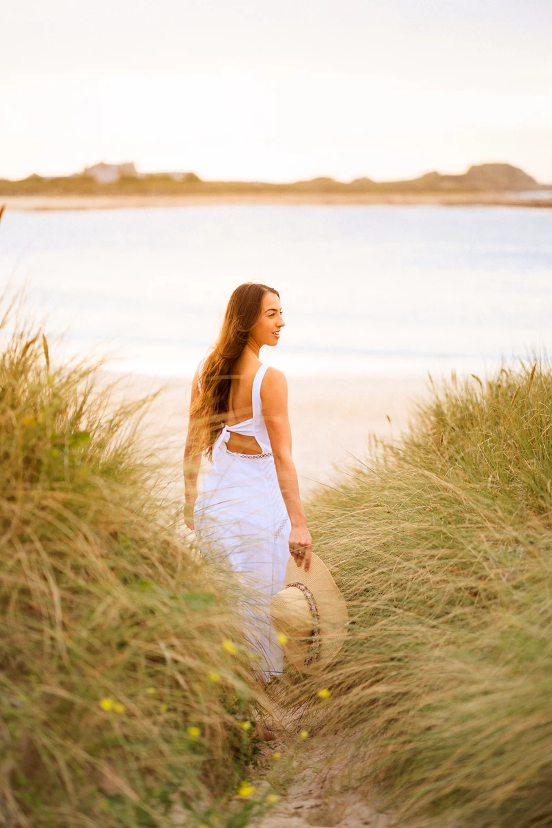 Colour photo of a person in a dress standing in a grassy area next to a body of water