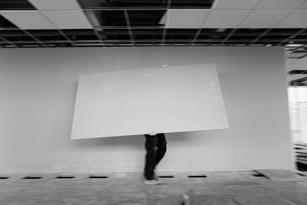 Black & white documentary style photo of man carrying plasterboard