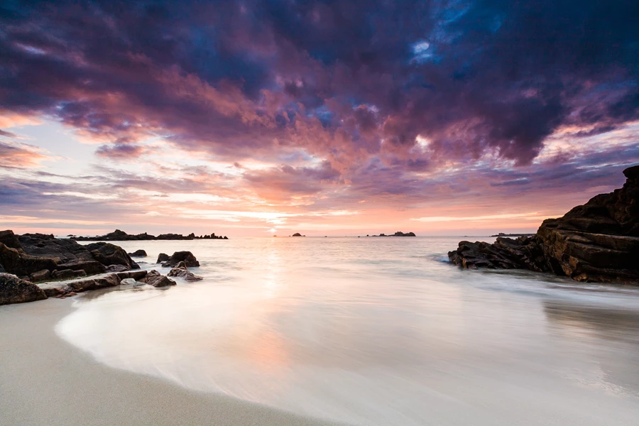 Landscape photo of beach scene with glossy wet sand and long exposure blurred water with sunset sky