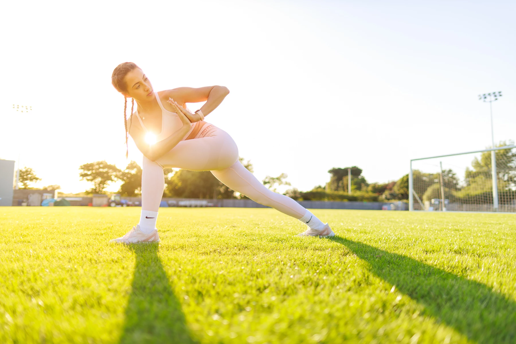 Colour photo of a person in a white leotard stretching on grass