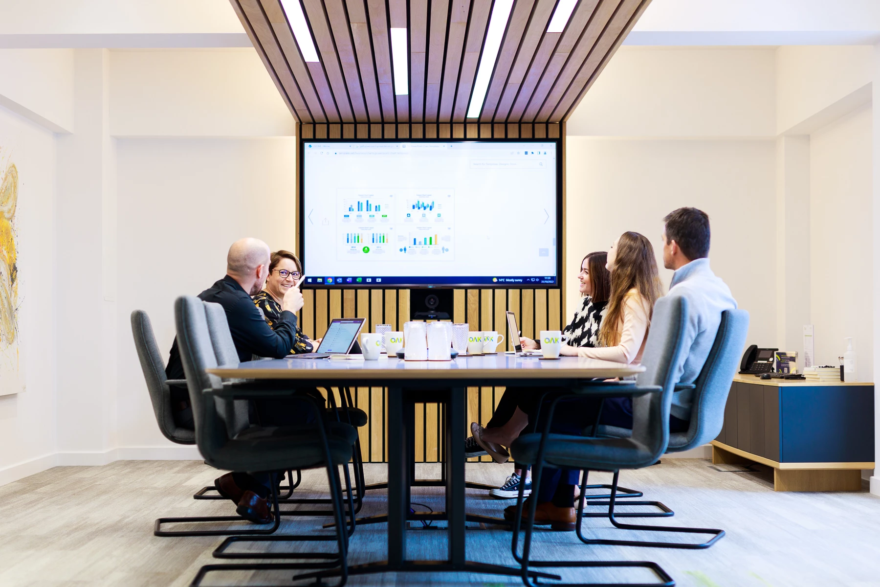 Colour photo of a group of people sitting around a table looking at a screen