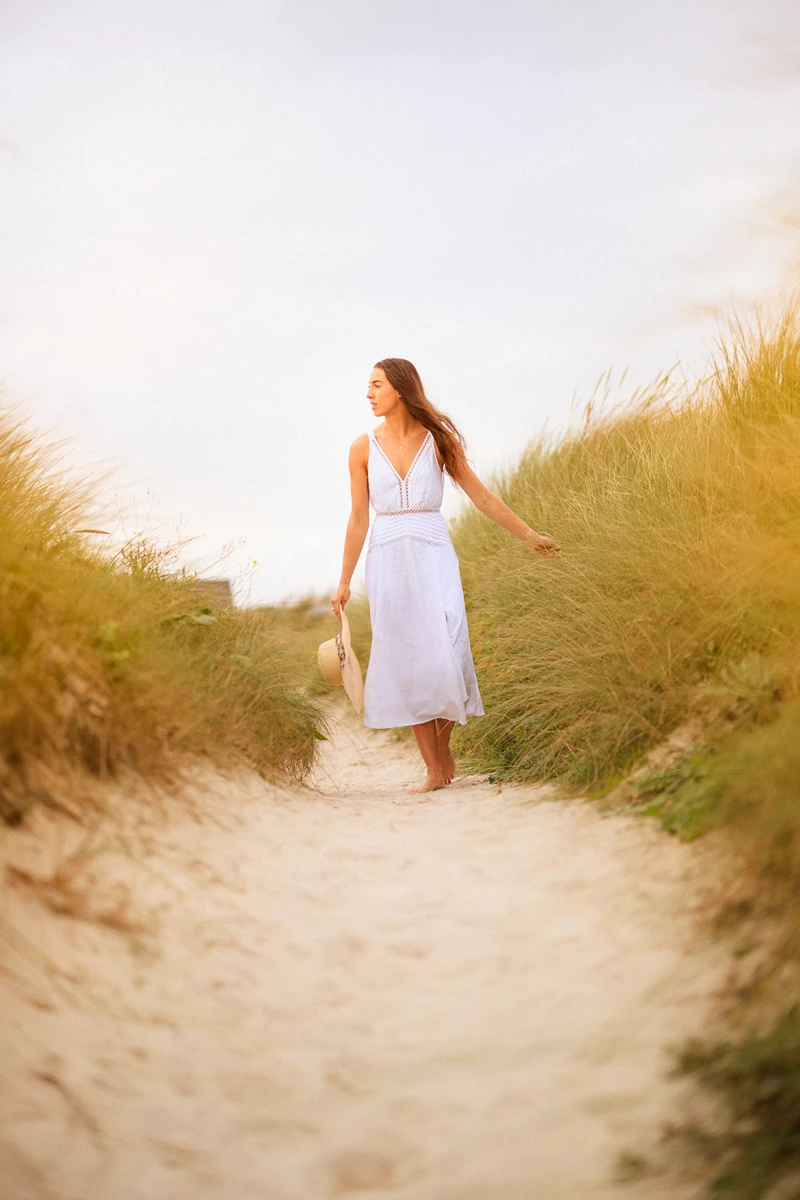 Colour photo of a person in a white dress walking on a sandy beach