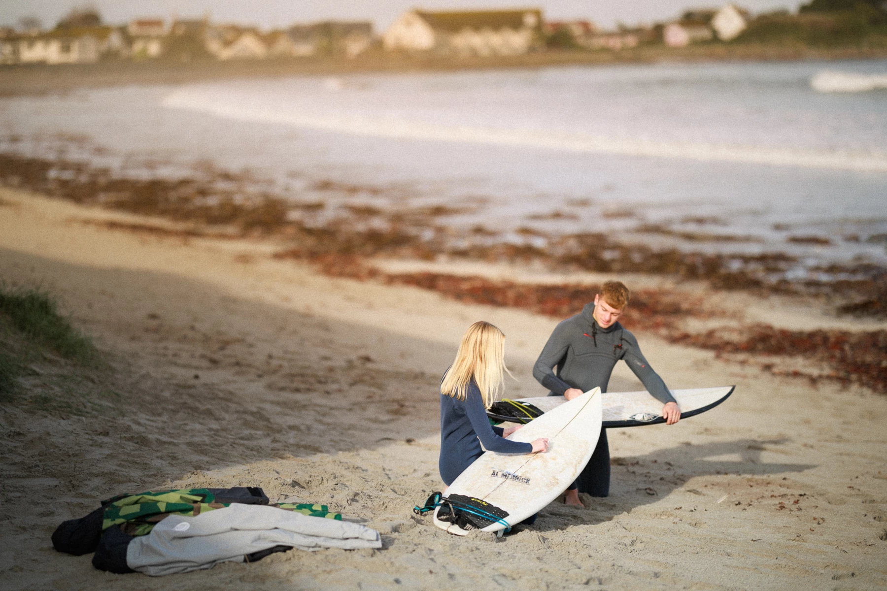 Colour photo of a couple of people stand on a beach with surfboards