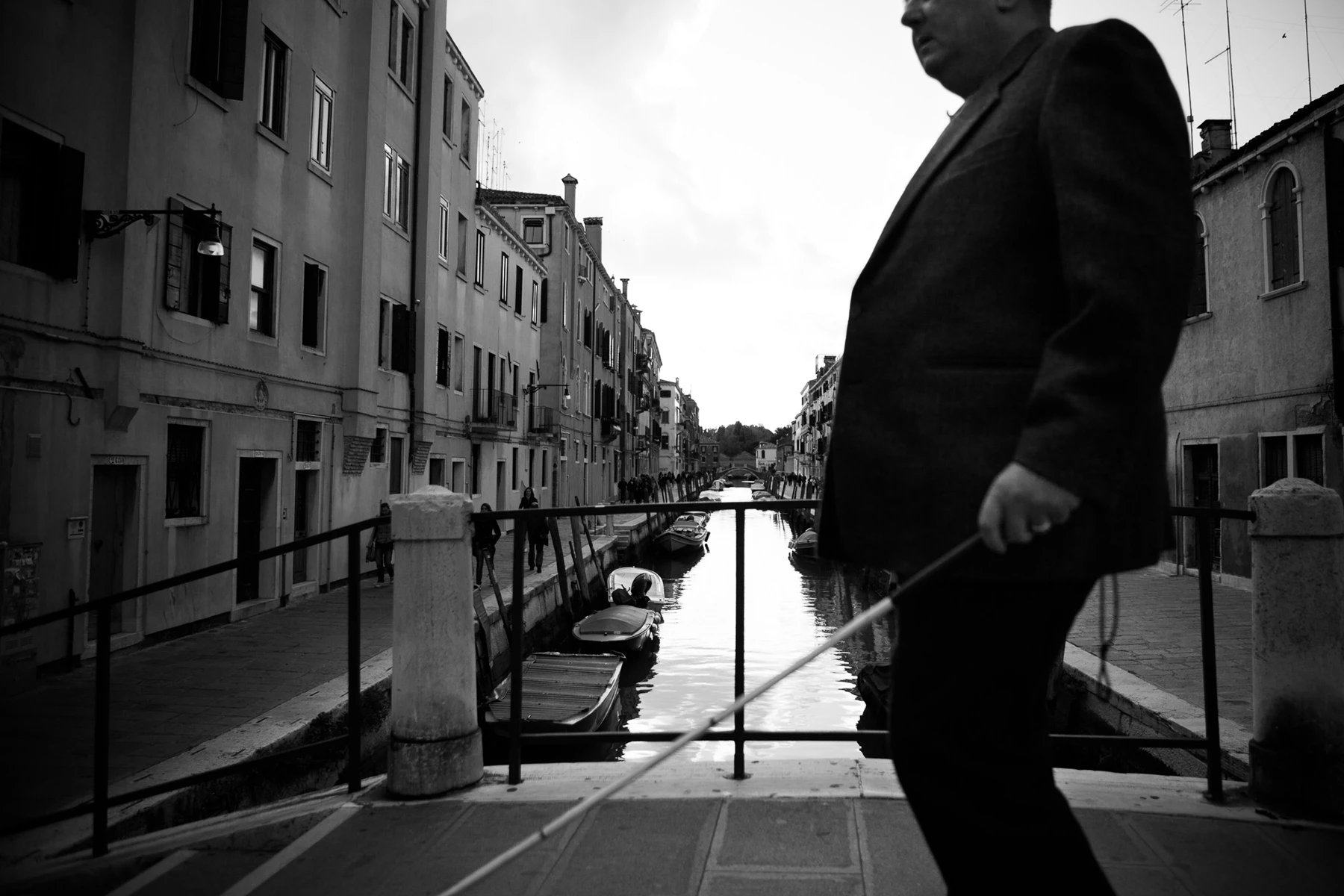 Black & white photo of a man walking on a bridge