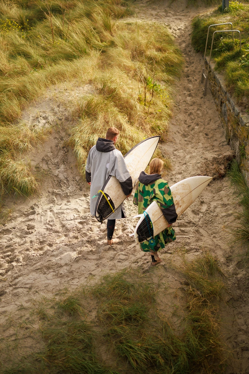 Colour photo of a couple of people carrying surfboards