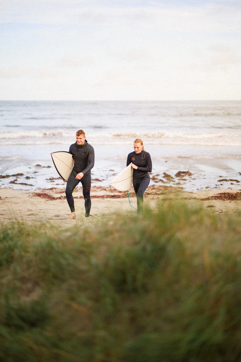 Colour photo of a couple of women carrying surfboards on a beach