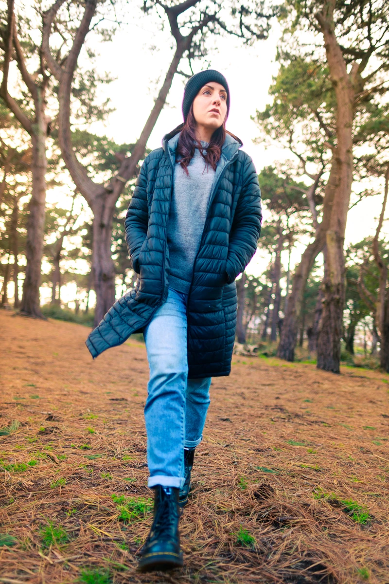 Colour photo of a person in a blue coat and hat holding a stick in a forest