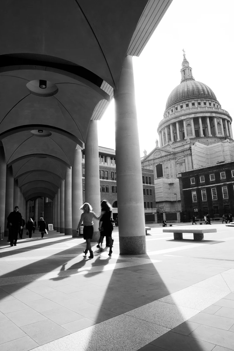 Black & white photo of a group of people walking under a large archway