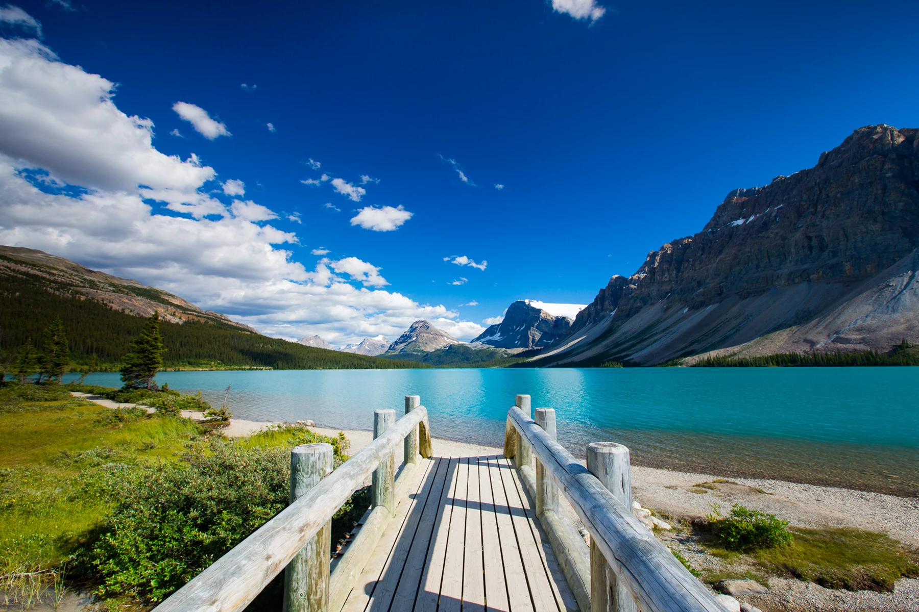 Colour photo of a wooden bridge over a body of water with mountains in the background