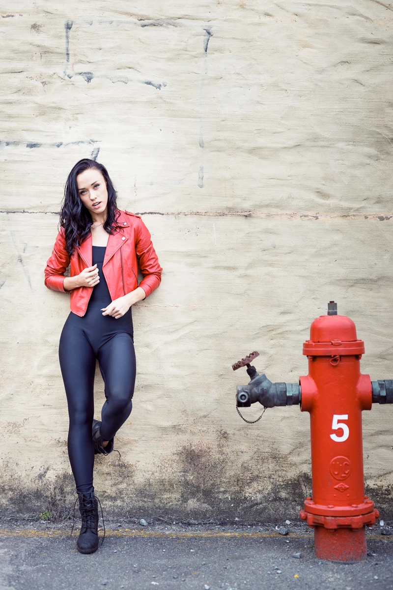Fashion photo of woman in red leather jacket against wall next to fire hydrant