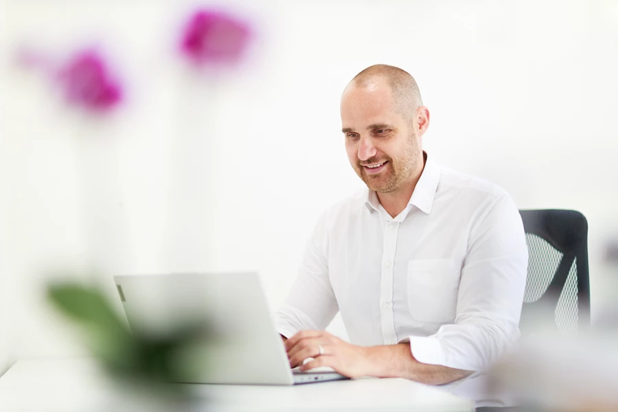Colour photo of a man sitting at a table with a laptop