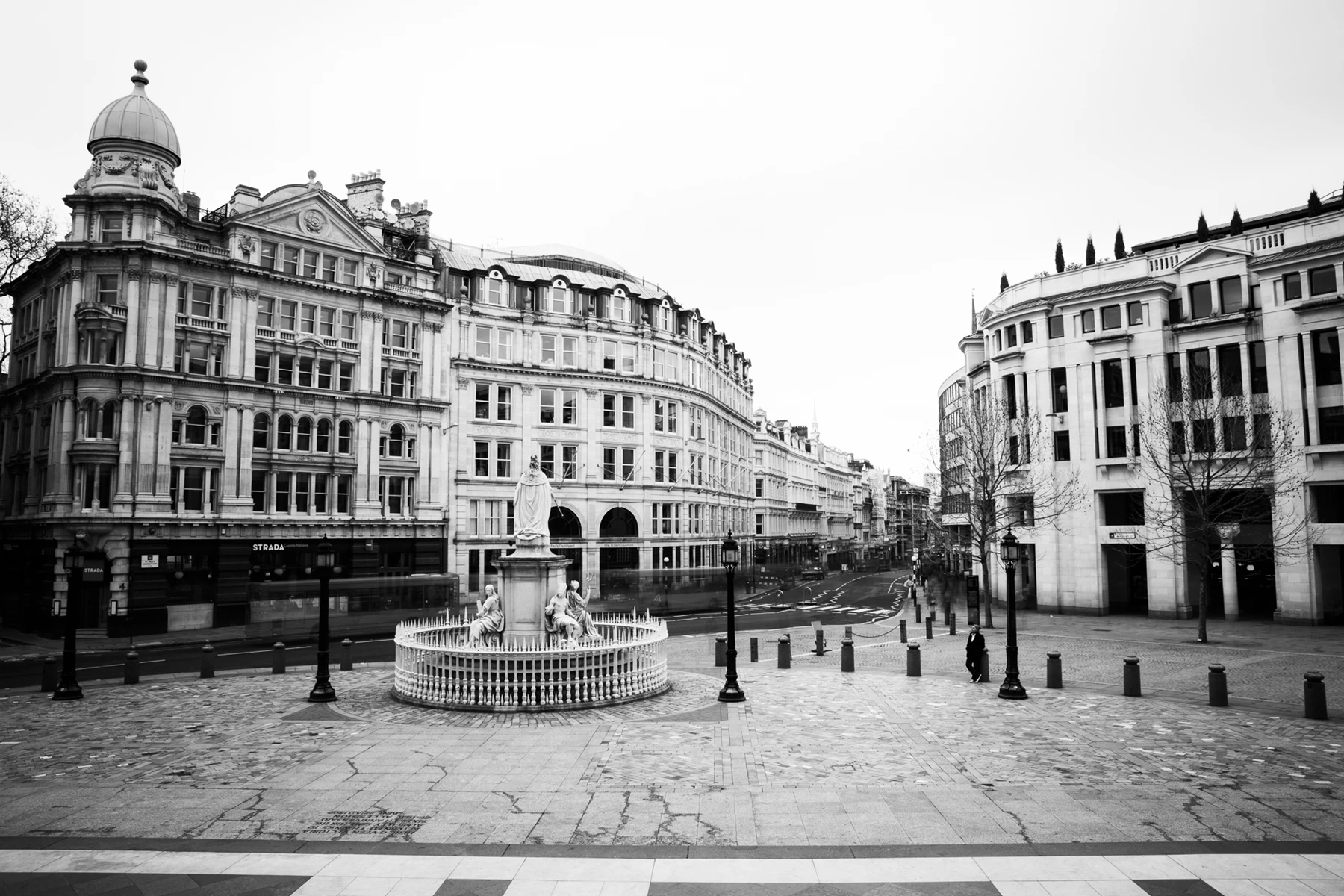 Black & white photo of a fountain in a courtyard with buildings in the background