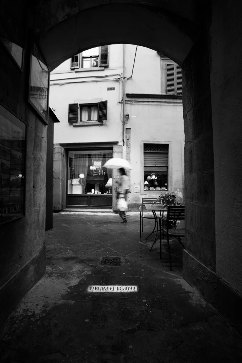 Black & white photo of a person walking down a sidewalk with an umbrella
