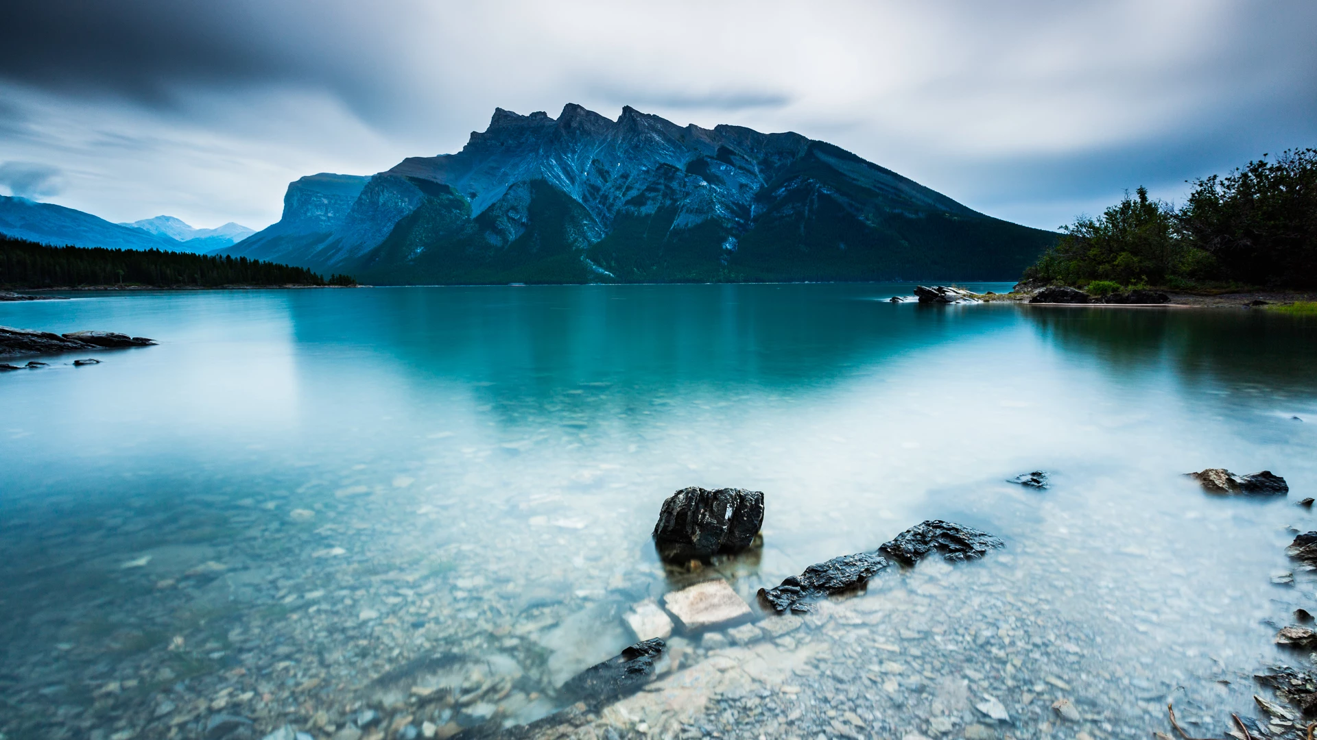 Colour photo of a body of water with rocks and mountains in the background