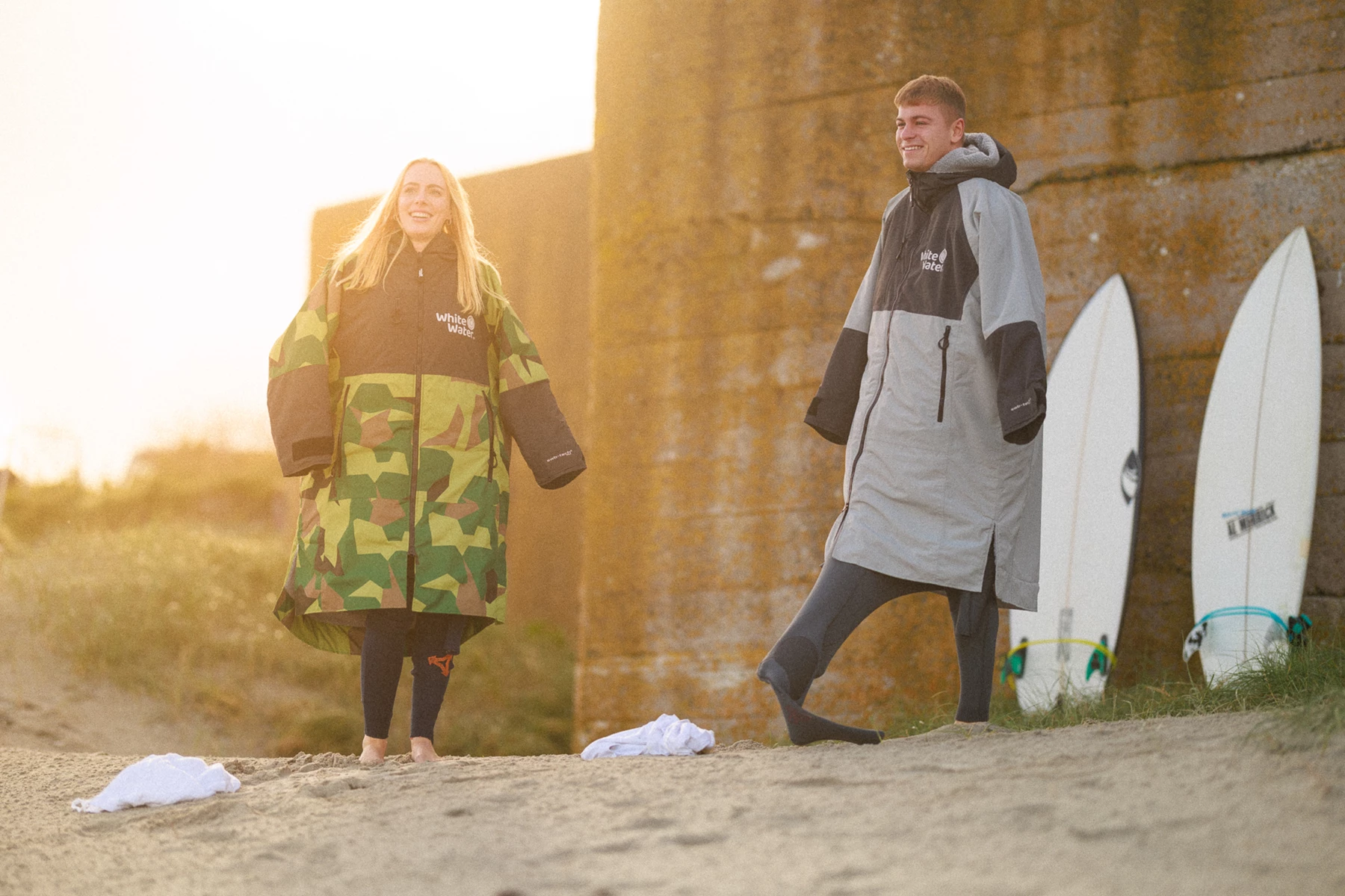 Colour photo of a man and woman standing next to surfboards